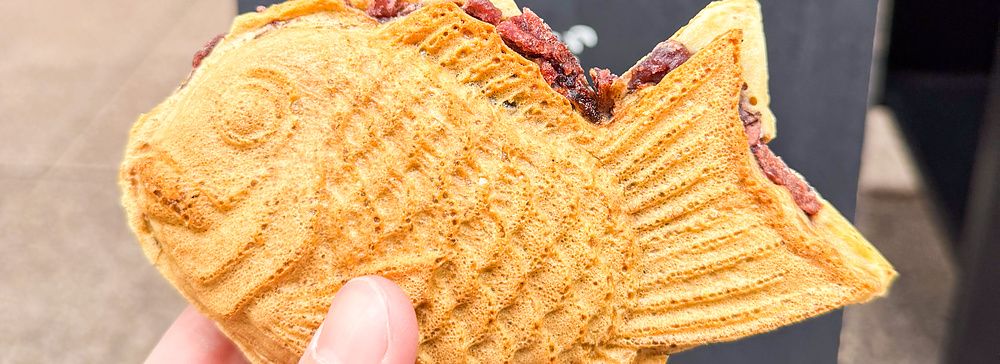 Un taiyaki tenuto in mano davanti all'insegna di Hakata Hiiragi Taiyaki a Fukuoka.