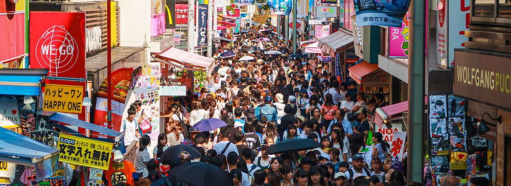 Strada affollata a Takeshita Dori con negozi e cartelli colorati.