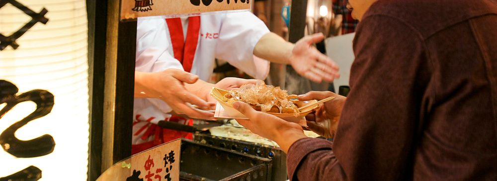 Una persona prende un piatto di takoyaki da una bancarella a Osaka.