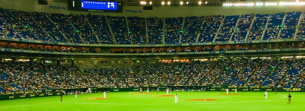 Partita di baseball al Tokyo Dome con spettatori e campo verde illuminato.