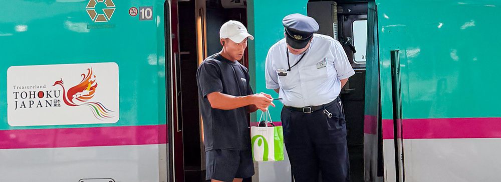 Persona interagisce con operatore ferroviario davanti a uno shinkansen alla stazione di Tokyo.