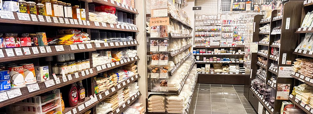Interno del negozio Tomizawa Shoten a Machida, con scaffali in legno pieni di prodotti alimentari e da pasticceria.