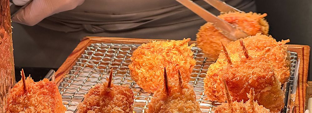 Chef che utilizza delle pinze per maneggiare pezzi di tonkatsu fritto su una griglia al Ginza Katsukami di Tokyo.