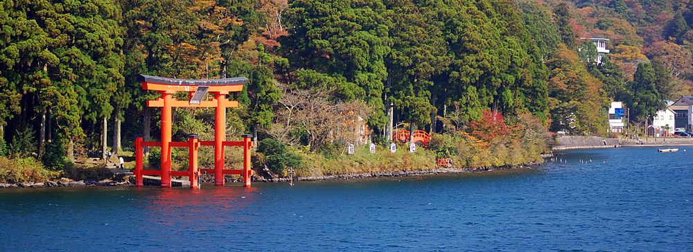 Un torii rosso sul Lago Ashi in Giappone, circondato da alberi.