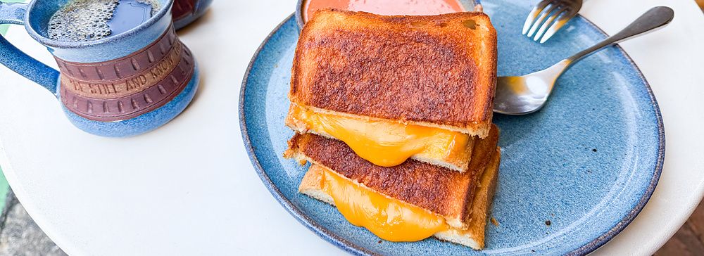 Un tost con formaggio a RoJean, Tokyo, servito su un piatto blu con caffè e una ciotola di zuppa su un tavolo bianco.