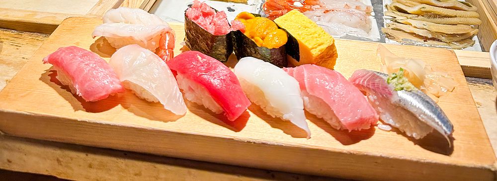Uno chef prepara il pesce dietro il bancone presso il ristorante Tsukiji Itadori Bekkan, con nigiri sushi in primo piano.