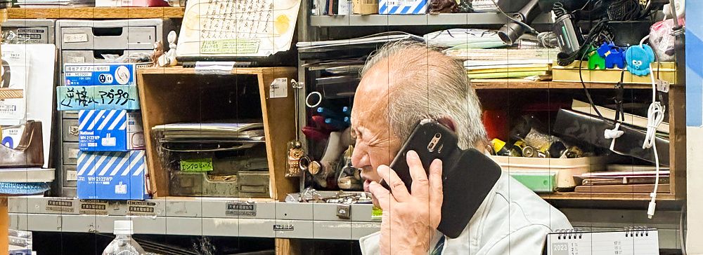 Uomo anziano al telefono in piccolo ufficio giapponese affollato.