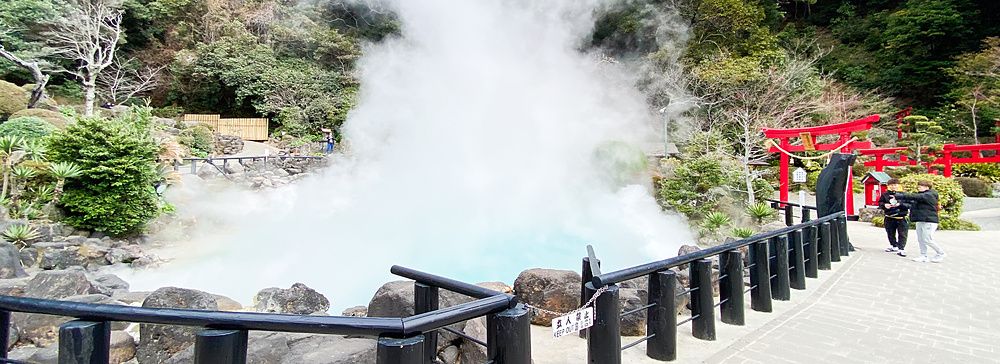 L'Umi Jigoku a Beppu con vapore denso che si alza dalla vasca azzurra accanto a un portale torii rosso.