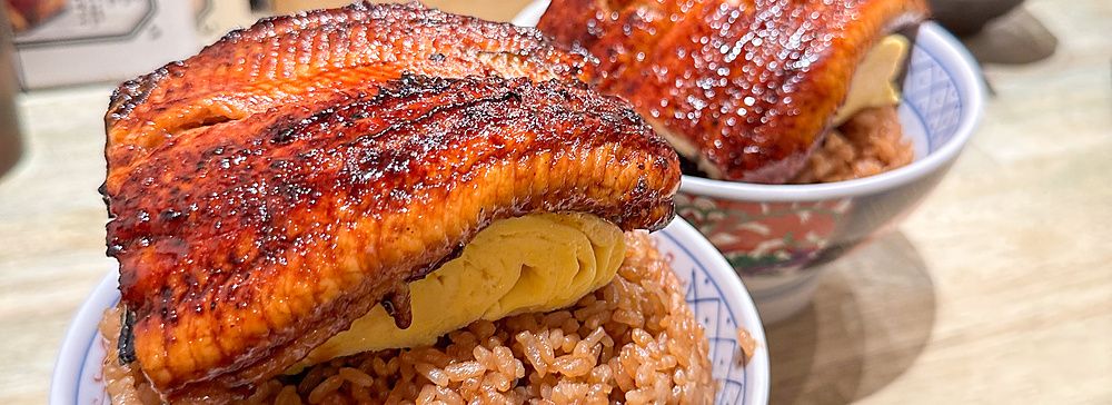 Due ciotole di riso con unagi e tamagoyaki servite su un bancone di legno all'interno del ristorante Izumo a Osaka.