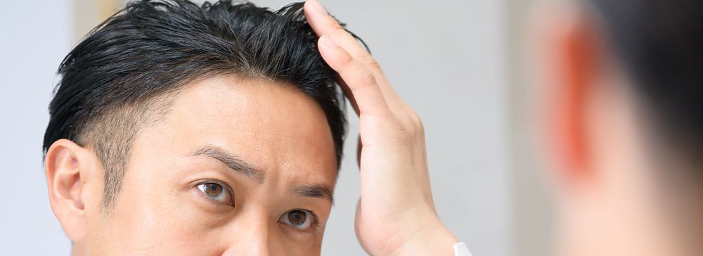 Uomo con camicia bianca e cravatta che si sistema i capelli davanti a uno specchio in un ambiente interno.