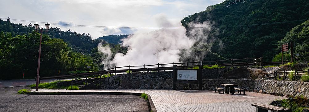 Vapore termale che sale da una foresta vicino a un piazzale in pietra con panchine a Kirishima, Giappone.