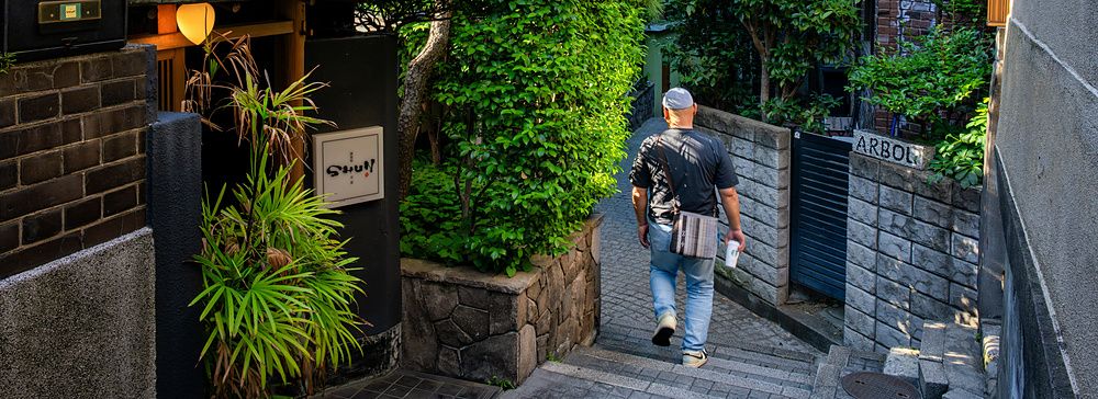Uomo che scende i gradini di un vicolo pittoresco a Kagurazaka, Tokyo, circondato da piante e case tradizionali.