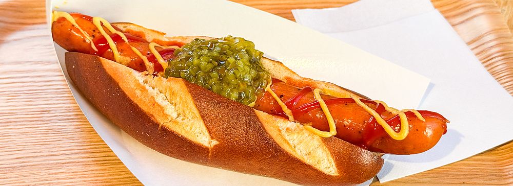 Un hot dog con pane tipo pretzel, senape, ketchup e cetriolini servito su un vassoio di legno da König a Kichhijoji.