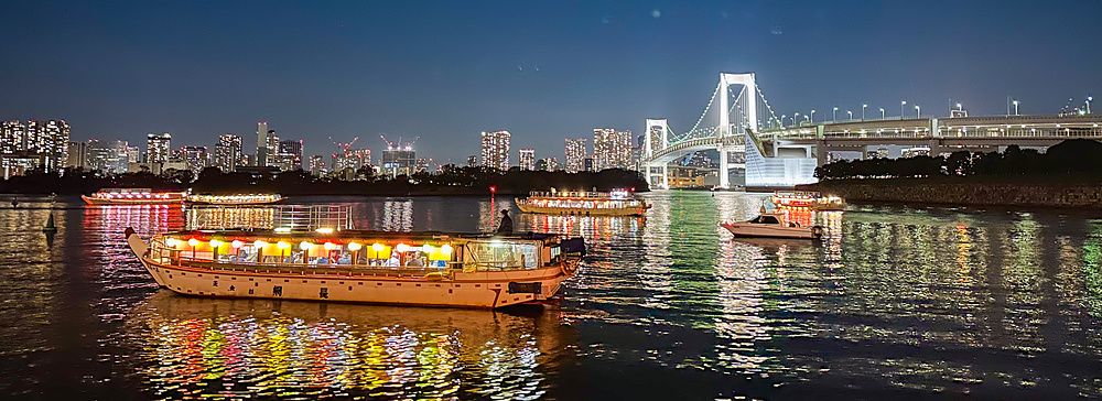 Una Yakatabune a Tokyo naviga nella baia di notte con il Rainbow Bridge illuminato sullo sfondo.