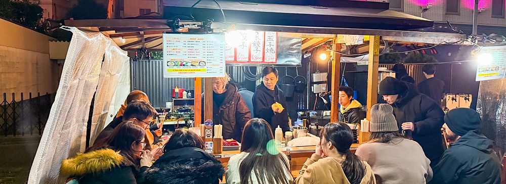 Persone sedute attorno a un bancone in uno yatai a Fukuoka, una tipica bancarella di cibo su strada illuminata la sera.