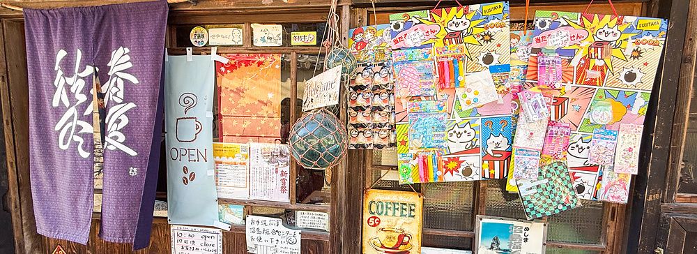 Facciata in legno dello Yoshijin Battari Cafe sull'isola di Nushima con un noren viola e insegne colorate.