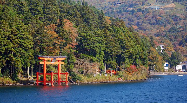 Un torii rosso sul Lago Ashi in Giappone, circondato da alberi.