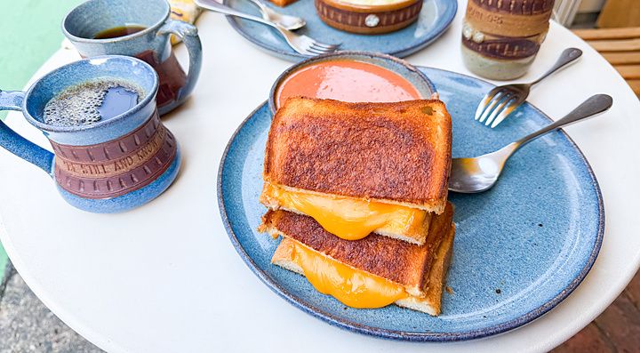 Un tost con formaggio a RoJean, Tokyo, servito su un piatto blu con caffè e una ciotola di zuppa su un tavolo bianco.