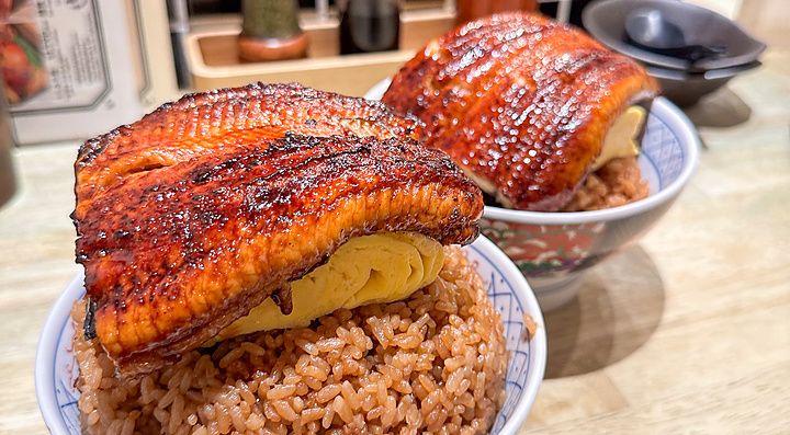 Due ciotole di riso con unagi e tamagoyaki servite su un bancone di legno all'interno del ristorante Izumo a Osaka.