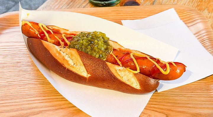 Un hot dog con pane tipo pretzel, senape, ketchup e cetriolini servito su un vassoio di legno da König a Kichhijoji.