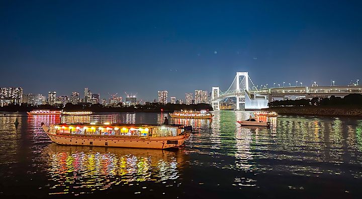 Una Yakatabune a Tokyo naviga nella baia di notte con il Rainbow Bridge illuminato sullo sfondo.