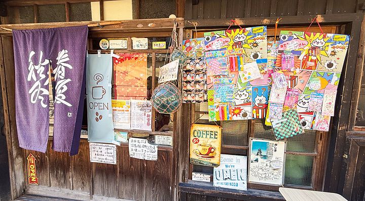 Facciata in legno dello Yoshijin Battari Cafe sull'isola di Nushima con un noren viola e insegne colorate.
