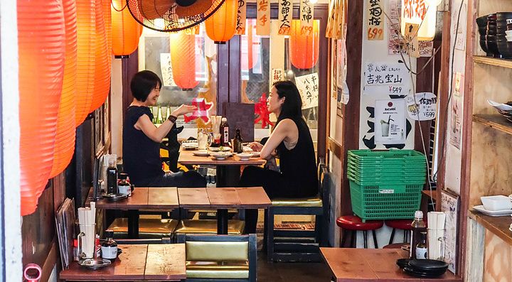 Interno di un piccolo izakaya a Yurakucho Yokocho con lanterne rosse e due persone sedute ai tavoli in legno.