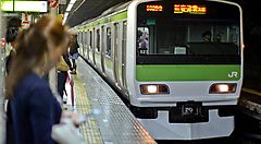 Un treno Yamanote Line alla stazione con persone in attesa sul binario.