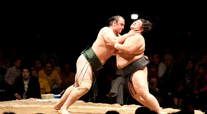 Due lottatori di sumo durante un incontro sul ring circondati dal pubblico.