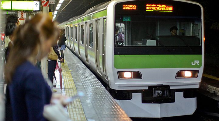 Un treno Yamanote Line alla stazione con persone in attesa sul binario.