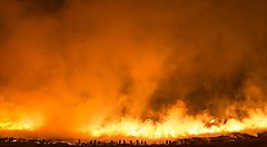 Un vasto incendio notturno con fiamme e fumo arancioni.
