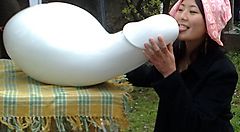 Una donna con fazzoletto rosa interagisce con una scultura bianca astratta su un tavolino all'aperto.