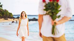Un ragazzo in spiaggia, con delle rose dietro la schiena, fa una sorpresa ad una ragazza.