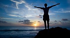 Silhouette di un ragazzo da solo al tramonto, su uno scoglio.