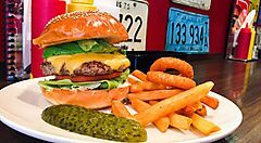 Hamburger con patatine fritte e anelli di cipolla su un piatto bianco.