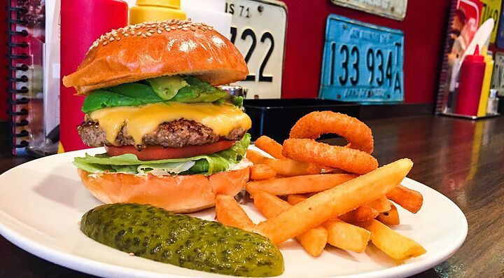 Hamburger con patatine fritte e anelli di cipolla su un piatto bianco.