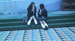 Due ragazze sedute su gradini mangiano gelato, indossando uniformi scolastiche e scaldamuscoli bianchi.