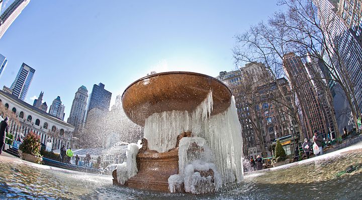 Fontana ghiacciata in un parco urbano con grattacieli sullo sfondo.