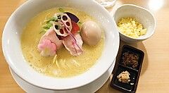 Ramen con uovo e guarnizioni colorate in una ciotola bianca su un tavolo di legno.