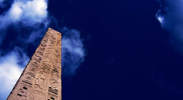 Un obelisco antico si staglia contro un cielo blu con nuvole sparse.