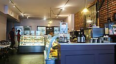 Interno di una caffetteria con vetrine piene di dolci e tavoli.