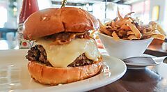 Hamburger con formaggio e cipolle caramellate, accompagnato da patatine fritte.