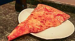 Fetta di pizza su piatto di carta, con bottiglia sullo sfondo.