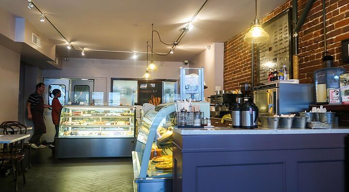 Interno di una caffetteria con vetrine piene di dolci e tavoli.