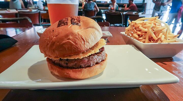 Burger umami su piatto bianco con patatine fritte e bicchiere di birra sullo sfondo.