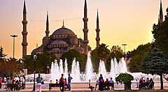 La Moschea Blu di Istanbul al tramonto con fontane e visitatori in primo piano.