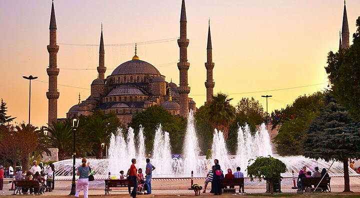 La Moschea Blu di Istanbul al tramonto con fontane e visitatori in primo piano.