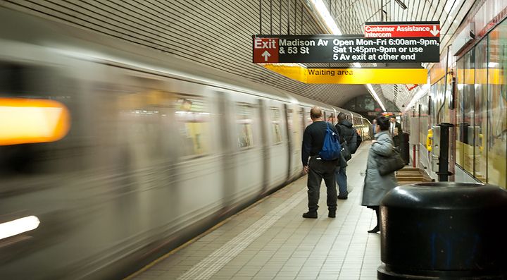 Persone in attesa su una banchina della metropolitana, treno in movimento.