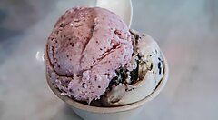 Coppetta di gelato con due gusti, uno rosa e uno con pezzi di biscotto, su tavolo di marmo.