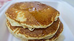 Due pancake impilati con sciroppo serviti su un piatto bianco.